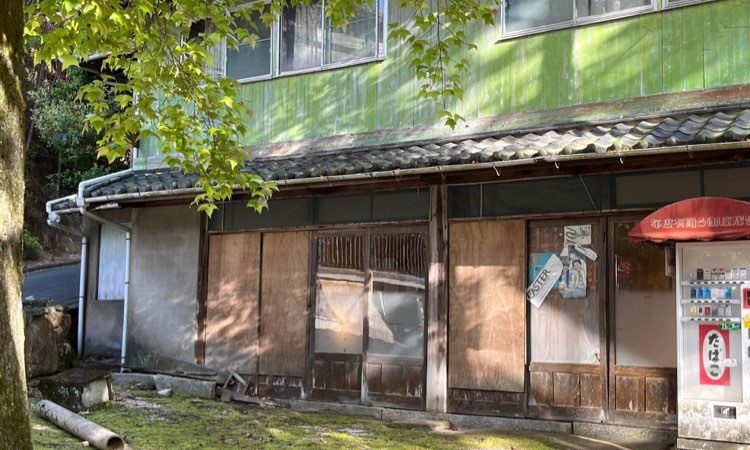 Vieille maison en bois vert qui semble abandonnée, avec un vieux distributeur de tabac