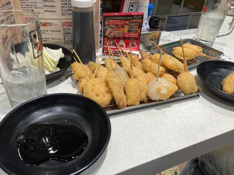 Une vingtaine de kushi katsu (brochettes frites), spécialité locale, avec sa sauce épaisse dans un petit bol